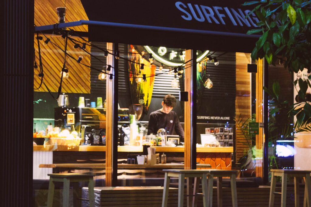 A business owner inside a surf-style coffee and juice shop in the evening, representing small businesses that use online music apps like Spotify or Pandora.
