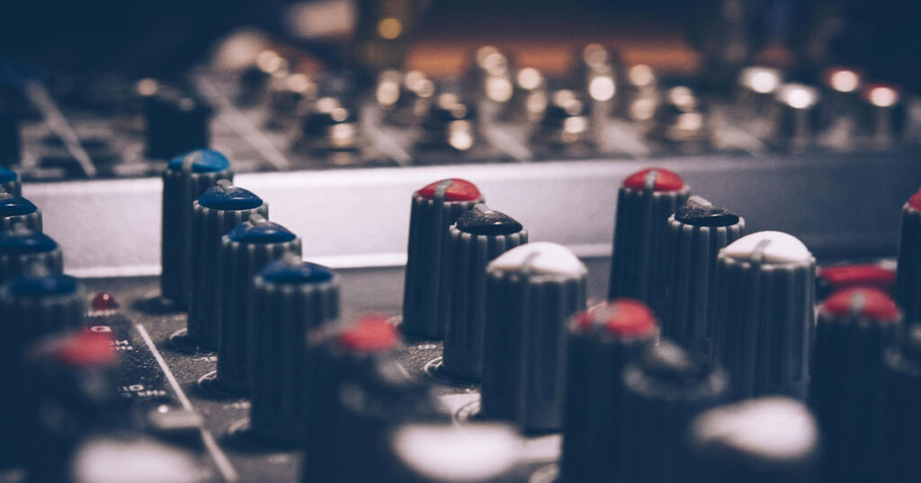 Close-up of volume knobs on a stereo mixing board, representing how businesses balance music volume for the right customer experience.