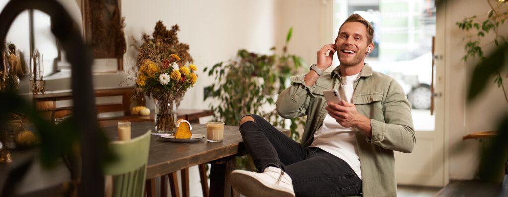 Man sitting in a café listening to music on his phone, illustrating personal music use in a business setting.